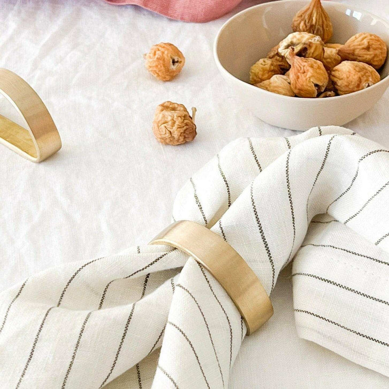 Set of four Rendr 100% linen striped olive napkins with gold napkin rings on white tablecloth