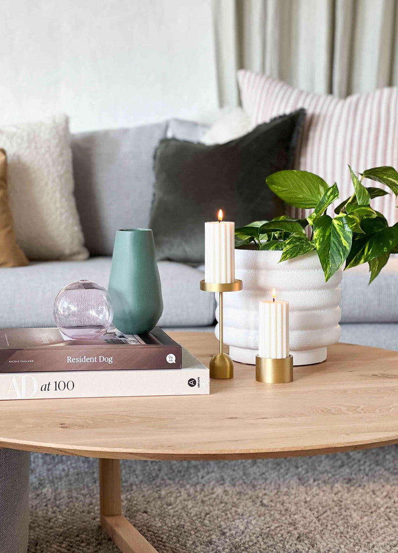 White matte porcelain Alder pot with a textured bubbly finish holding a green plant on a wooden coffee table with candles and decorative items in a cozy living room.