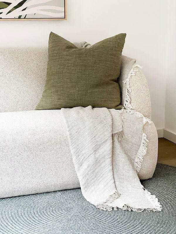 Olive norsu Studio Washable Cushion on beige sofa with light fringed throw blanket
