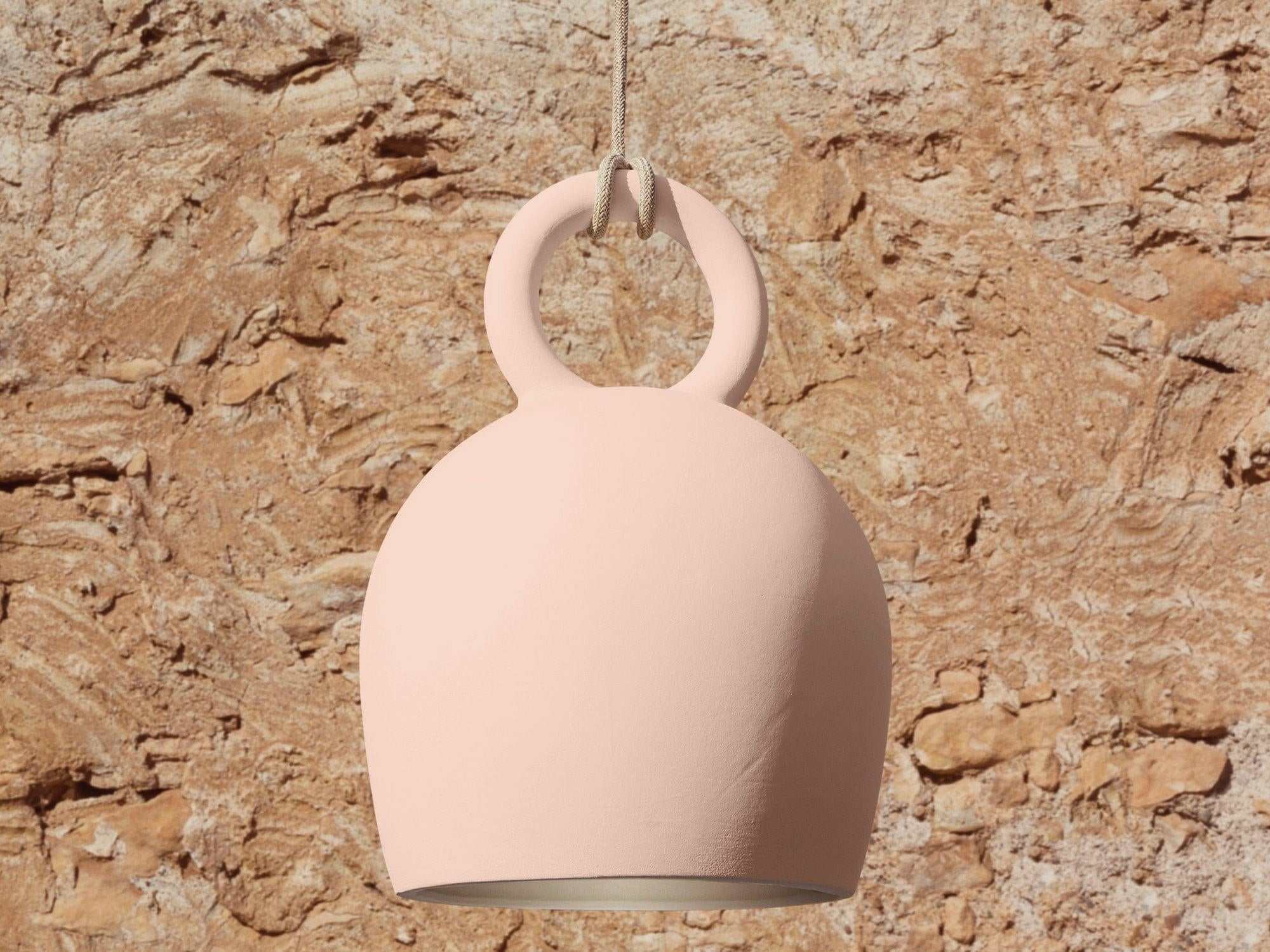 POTT Lighting Calo Pendant in salmon color with bell shape, handmade ceramic, hanging light fixture against rustic stone background