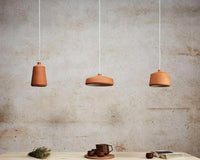 POTT Lighting Flame Pendant natural terracotta hanging lamps with white glazed interior in three shapes against textured wall