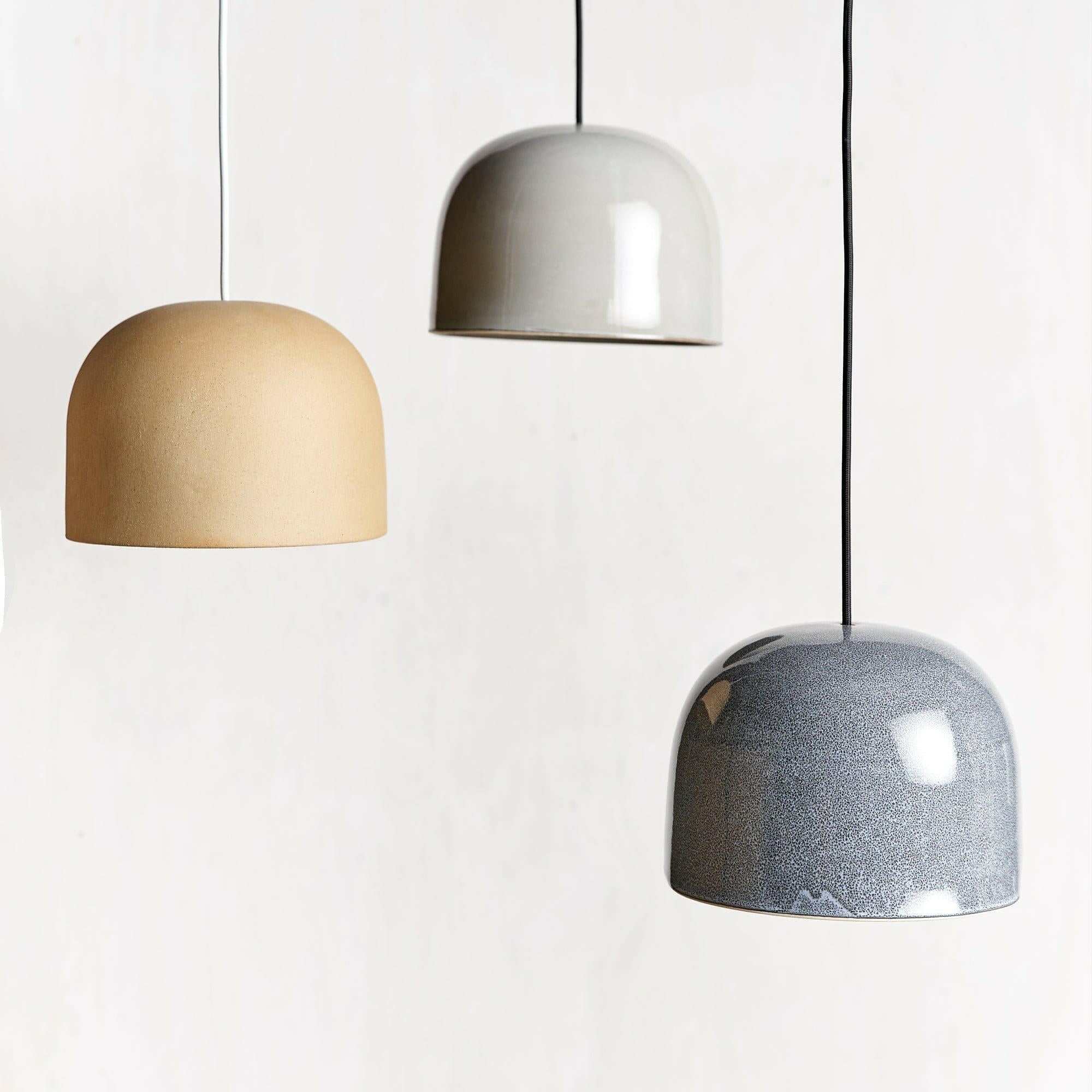 Three Robert Gordon Bell Light ceramic pendant lamps in beige, white, and gray colors hanging against a white background.