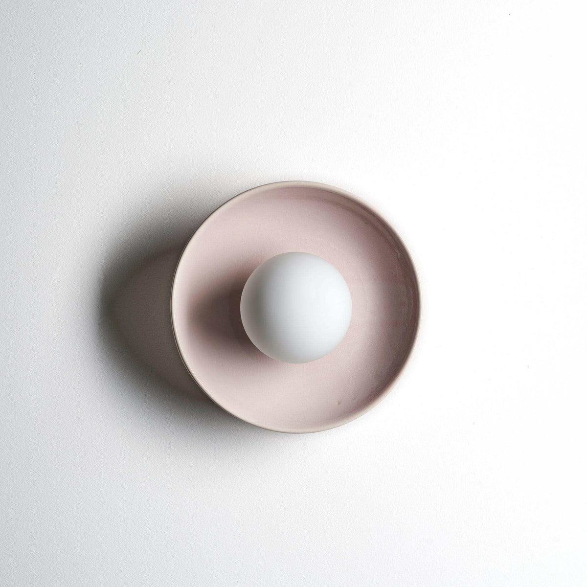 Robert Gordon Dish Wall Sconce in rose quartz ceramic with a round white bulb and minimalist design