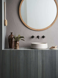 Robert Gordon Kiln 360 round hand basin in sand on modern bathroom countertop with round wooden mirror and decorative vases