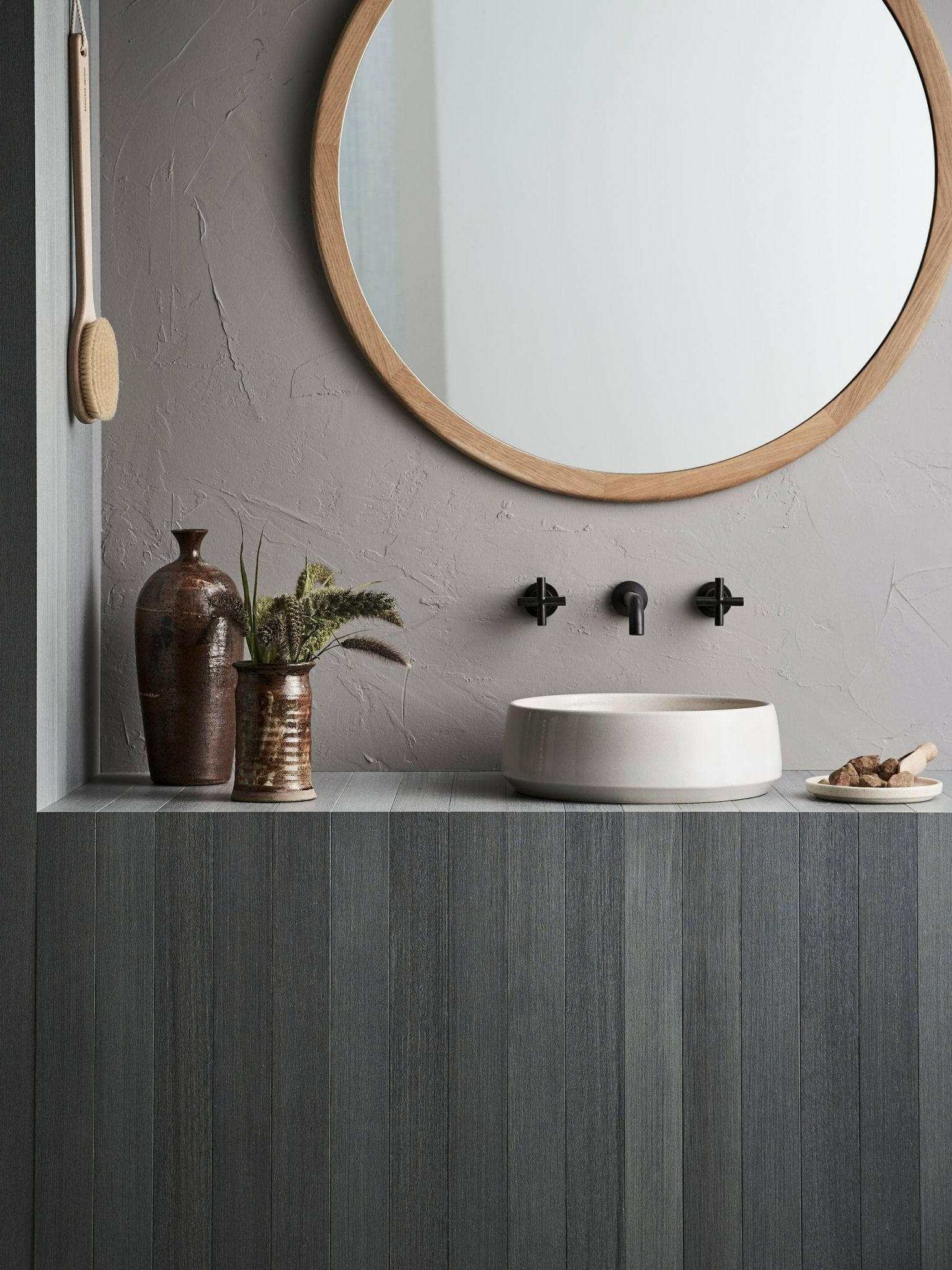 Robert Gordon Kiln 360 round hand basin in sand on modern bathroom countertop with round wooden mirror and decorative vases