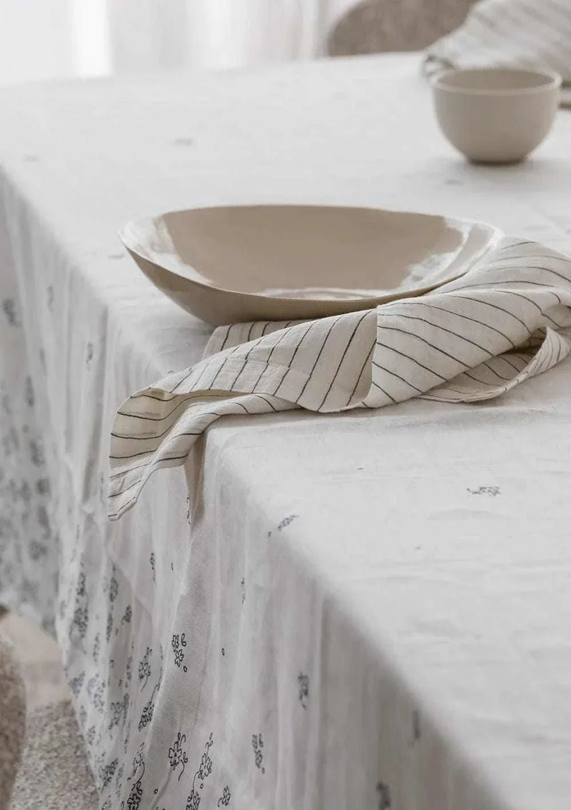 Set of four Rendr 100% linen striped olive napkins on a white patterned tablecloth with beige ceramic dishware