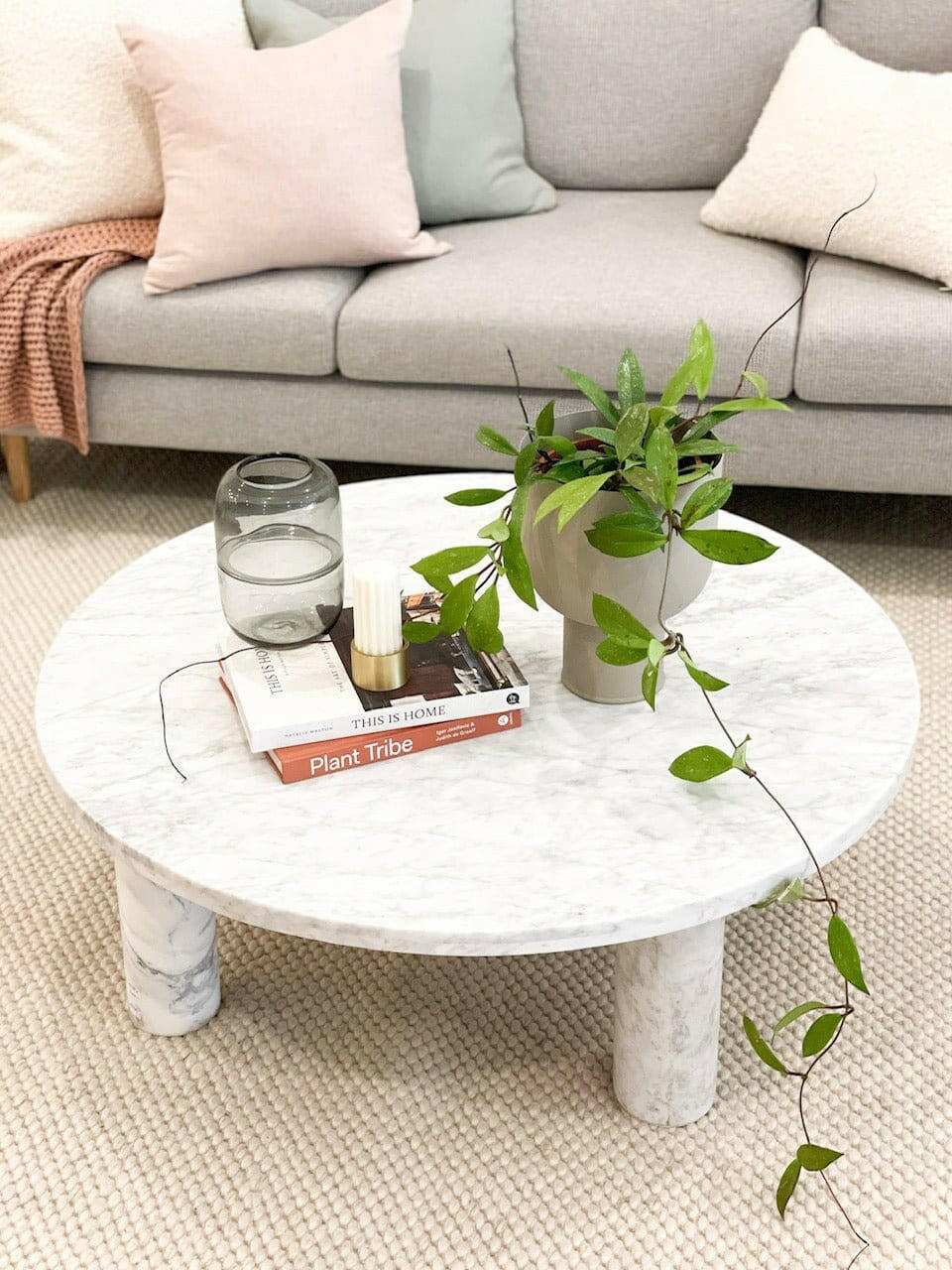Minimalist round marble coffee table styled with a plant, books, candle, and glass jar in a cozy living room setting.