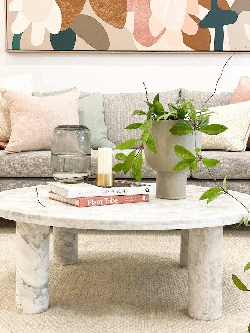 Modern marble coffee table styled with books, a glass jar, candle, and a green leafy plant in a beige pot in a cozy living room setting
