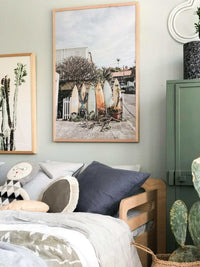 Summer Break Surfboard print wall art featuring surfboards outdoors in a wooden frame above a cozy bed with modern decor.