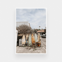 Summer Break Surfboard print featuring a row of colorful surfboards leaning against a fence in a coastal neighborhood, available in various sizes