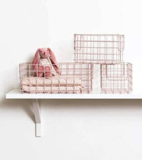 Set of three blush wire baskets in different sizes displayed on a white shelf with a pink stuffed rabbit inside the largest basket