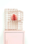 Set of blush pink wire baskets in varying sizes stacked on a pastel pink locker for organized storage