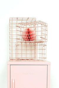 Set of blush pink wire baskets in varying sizes stacked on a pastel pink locker for organized storage