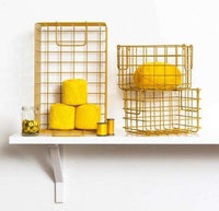 Set of mustard baskets in wireframe design with three yellow yarn balls and sewing thread on a white shelf