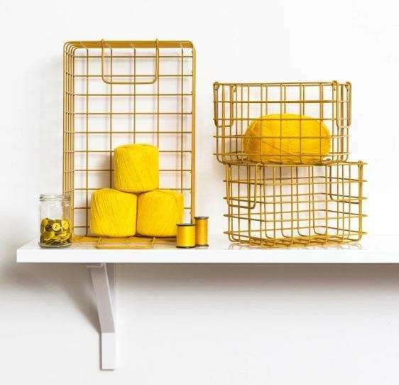 Set of mustard baskets in wireframe design with three yellow yarn balls and sewing thread on a white shelf