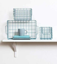 Set of Ocean baskets in blue wireframe design with one large and two smaller baskets arranged on a white wall shelf with books and a gray mug.