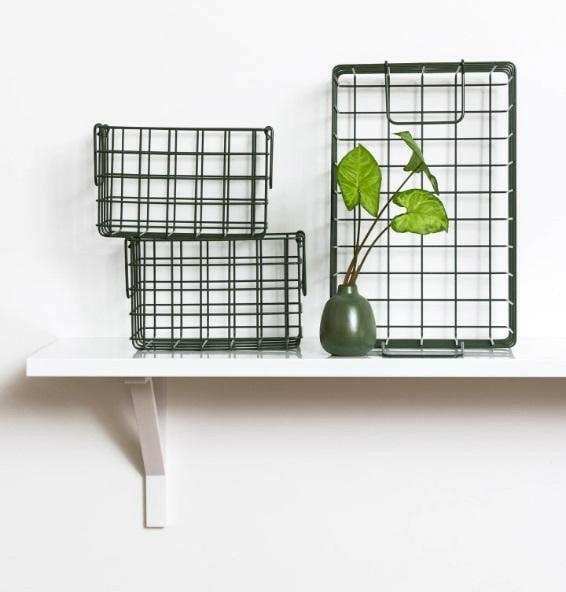Set of three olive baskets with metal grid design displayed on a white shelf with a small green vase and leafy plant.