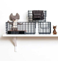 Set of three slate-colored wire baskets of varying sizes displayed on a white wall shelf for organized storage.