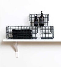 Set of three slate-colored metal storage baskets, including one large and two smaller baskets, displayed on a white shelf holding toiletries and towels