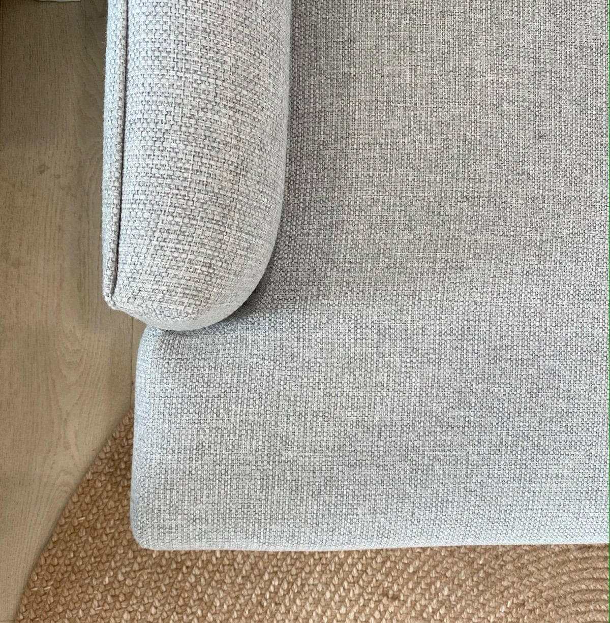 Close-up of Custom Norsu Sofa 2.5 seater armrest and cushion in Wells Driftwood fabric on woven rug.