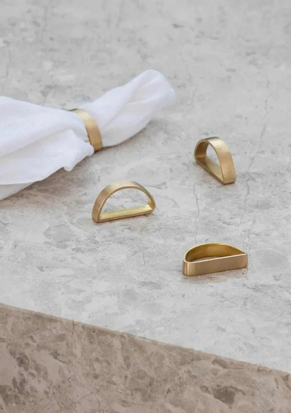 Set of four white Rendr 100% linen napkins with brass napkin rings on a stone surface